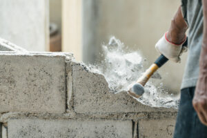 Someone using a hammer to demolition a cinderblock wall. 